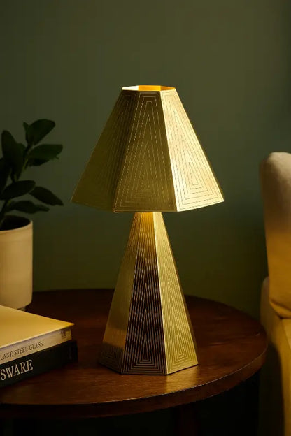 Gold table lamp on a wooden surface with a plant and book in the background